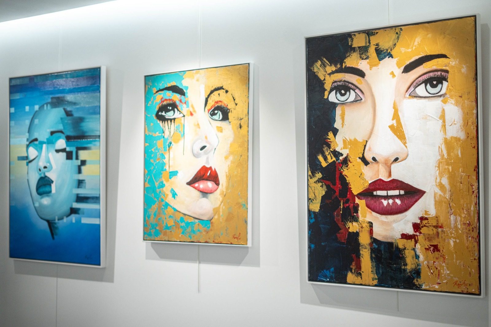 Three colorful portraits on a white gallery wall